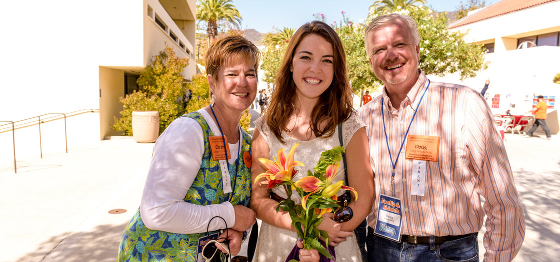 Student standing between two adults holding flowers - Pepperdine University