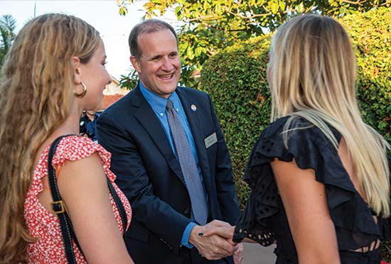 President Gash shaking hands with two students outside