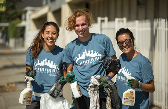 Three students outside holding cleaning supplies