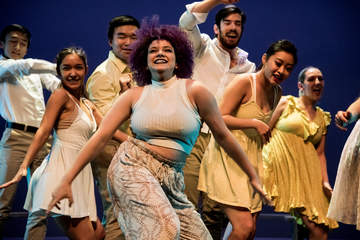 Students dancing and smiling in a group on stage