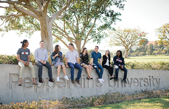 Eight students sitting outside on Pepperdine cement sign