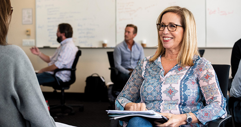 Professor sitting and smiling with notebook in lap in classroom