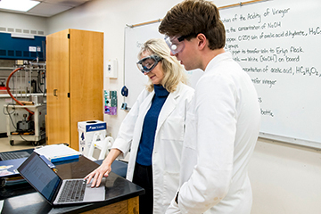 two people in lab coats and goggles looking at computer