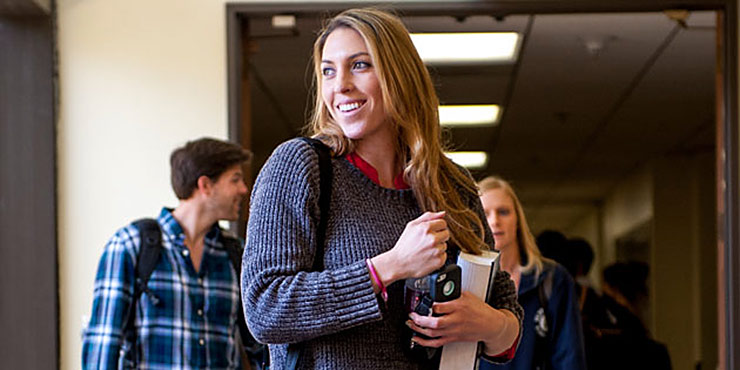 A student holding books smiles in the hallway - Pepperdine University