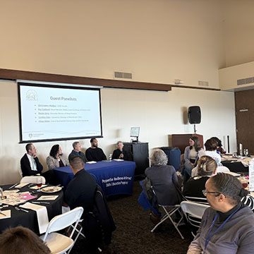 attendees at tables and chairs listening to a panel