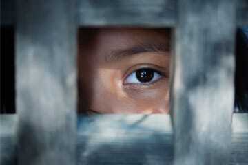 A female eye peers through a metal prison door