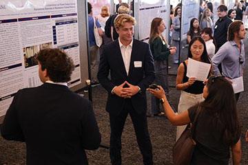 students in a crowd standing by symposium poster boards