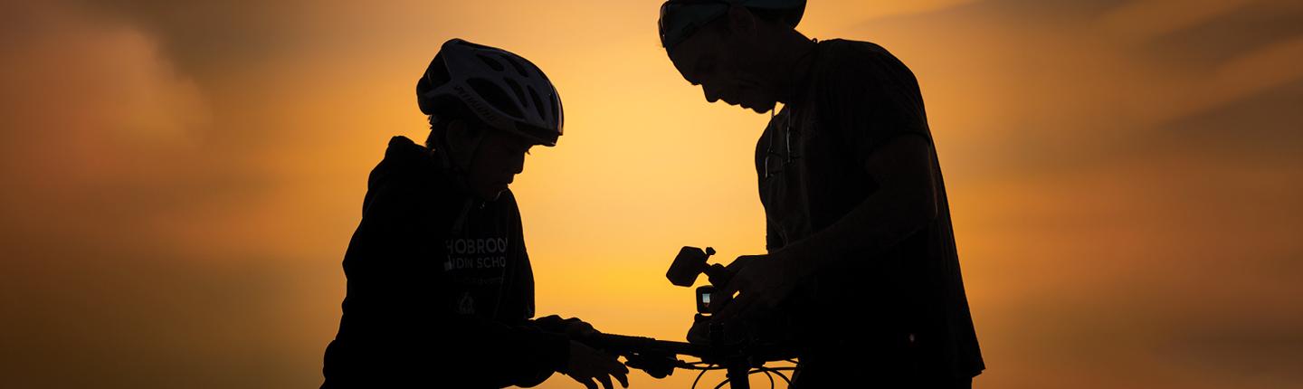 A child and an adult on bicycles silhouetted against a desert sunset
