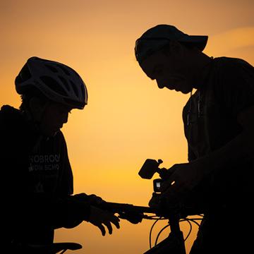 A child and an adult on bicycles silhouetted against a desert sunset