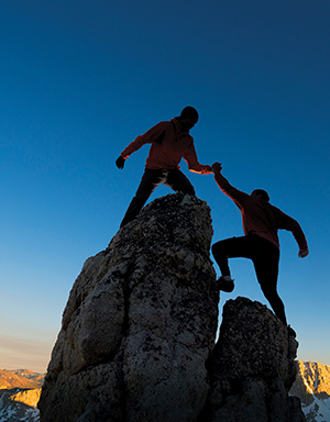 Two people climb mountain summit together