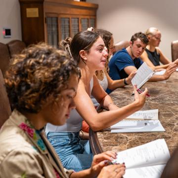 Students read from notebooks around a conference room table.