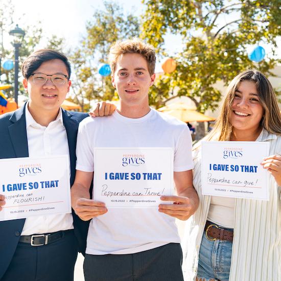 Three Pepperdine community members pose with signs on Pepperdine Gives day