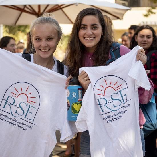 Two students holding up T-shirts with the RISE logo