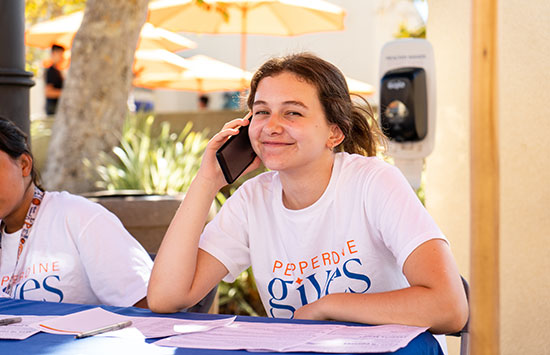 Student wearing a Pepperdine Gives shirt on the phone