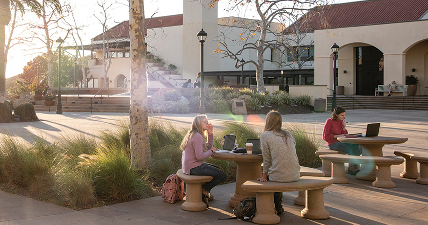 Students sitting at tables in Jocelyn Plaza at sunset