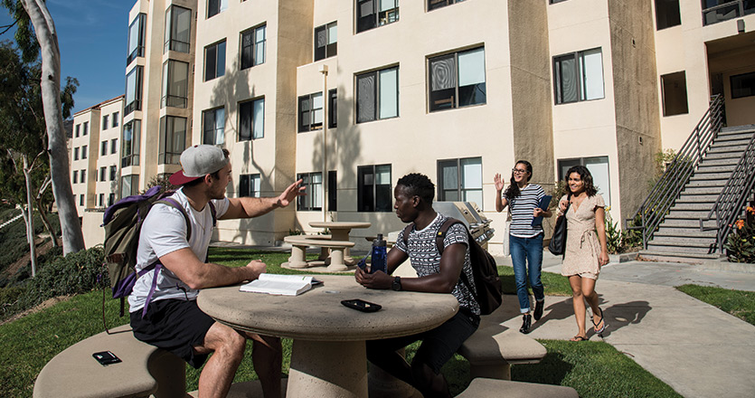 Students sitting outside at table waving to friends in the distance