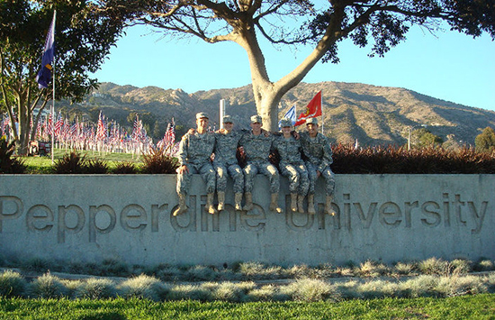Group of men sitting on Pepperdine sign with flags in background