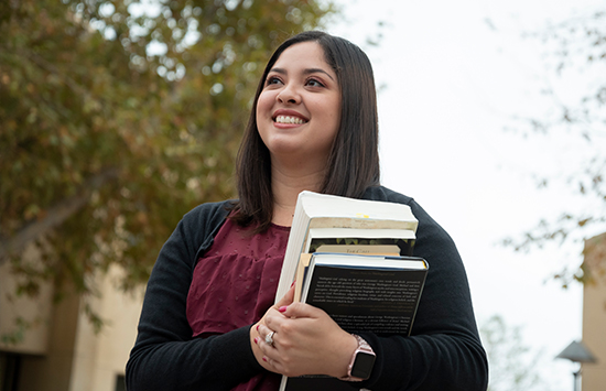 Student smiling holding books outside