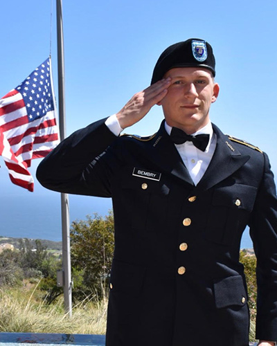 Student veteran Parker Bembry salutes with a flag in the background.
